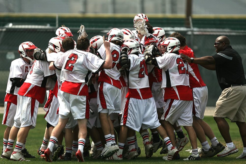 group of lacrosse players celebrating with coach during daytime